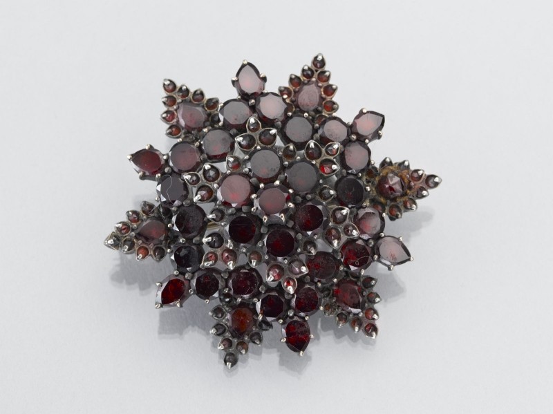 Stervormige broche van zilver, bezet met rode steentjes